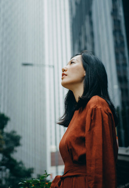 A woman in a red dress looks up at high-rise buildings.